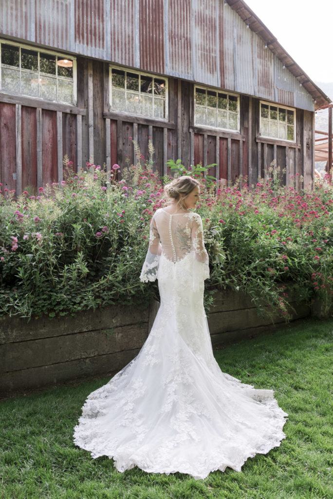 bride in vintage lace wedding dress in front of rustic barn and garden