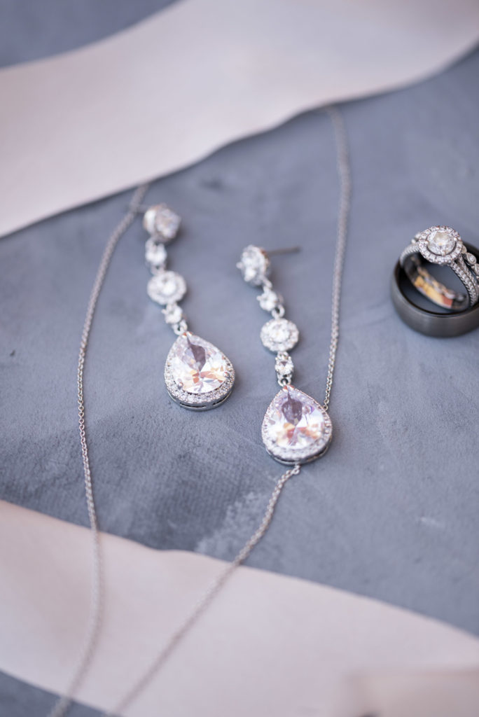 flat lay of bride's diamond earrings and wedding rings