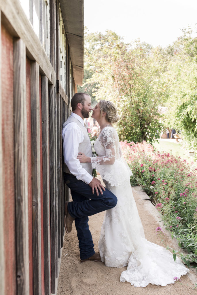 bride and groom kissing against rustic garden barn