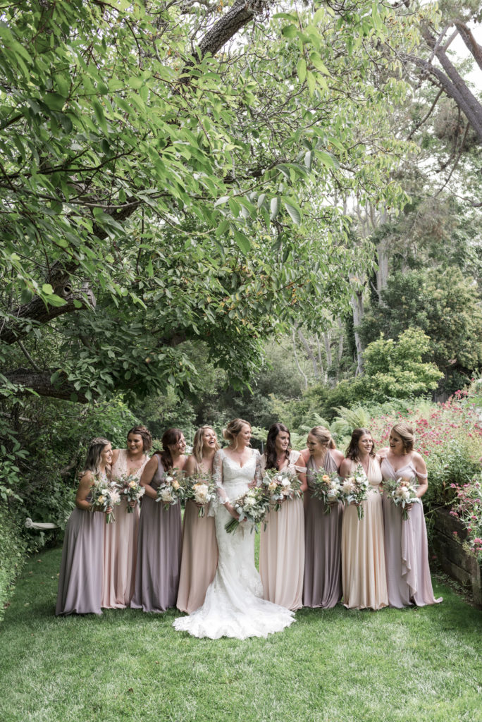 bride smiling with bridesmaids surrounded by greenery