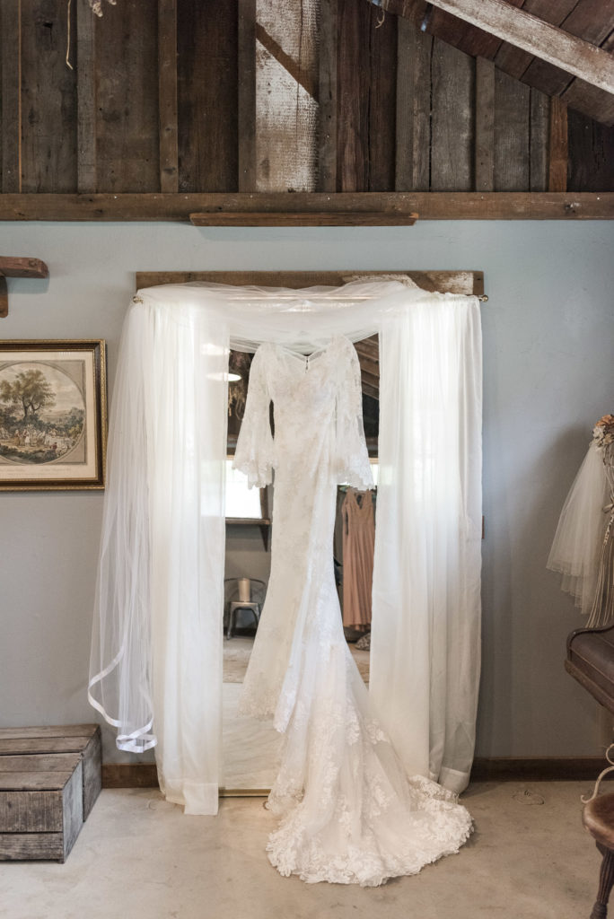 vintage lace wedding dress hanging on mirror in rustic barn