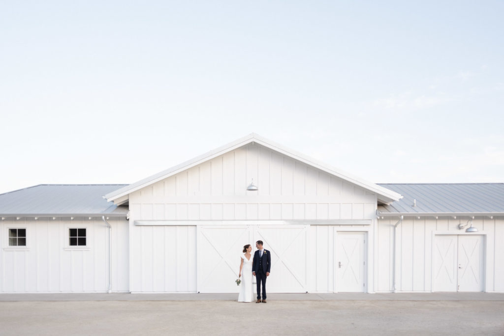bride and groom in front of new white barn wedding venue in San Luis Obispo by Kirsten Bullard Photography